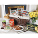 USA Irish Breakfast Basket. A woven picnic basket filled with packaged food items sits on a table. In front, a plate features bacon and sausages, alongside jars of jam and tea. A box of shortbread is also visible, along with scones and a small bouquet of yellow roses in the background. USA Irish Breakfast Basket. A woven picnic basket filled with packaged food items sits on a table. In front, a plate features bacon and sausages, alongside jars of jam and tea. A box of shortbread is also visible, along with scones and a small bouquet of yellow roses in the background.